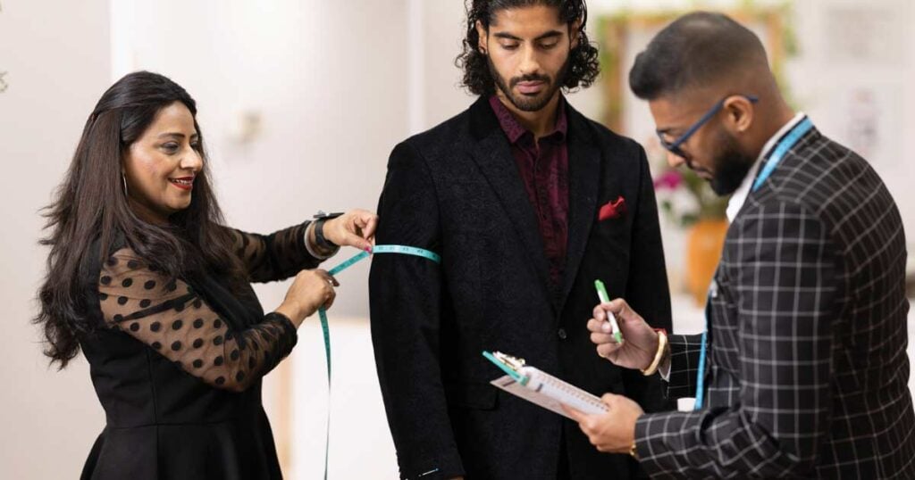 Tailor and assistant taking measurements for custom suit