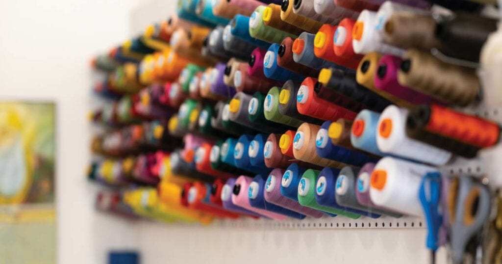 Dozens of large spools of thread on a wall of all colors