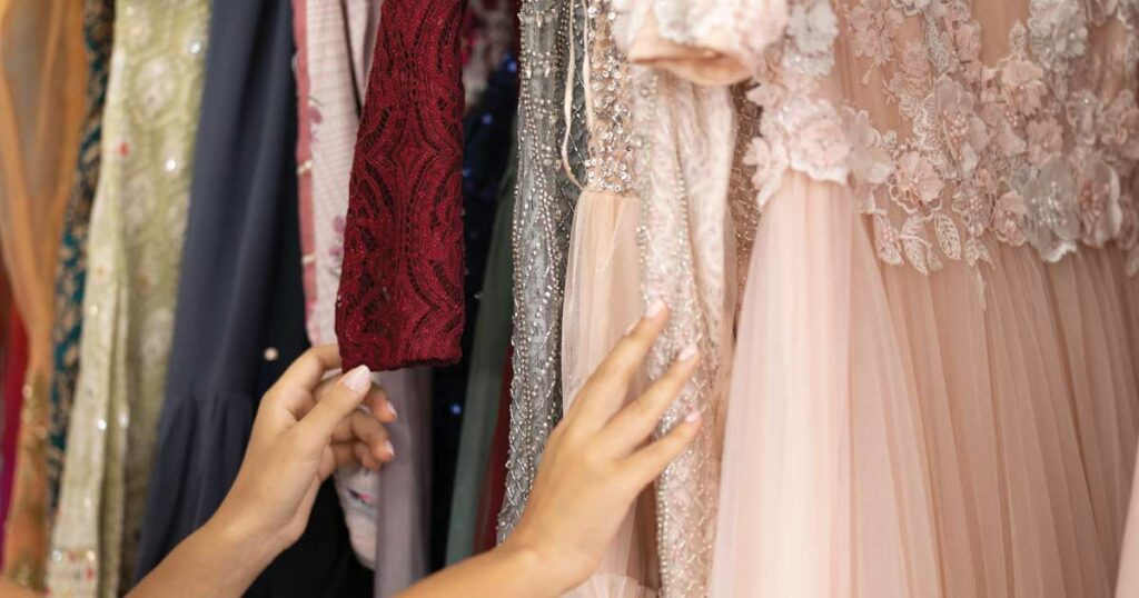 Women's hands looking through a variety of women's party dresses