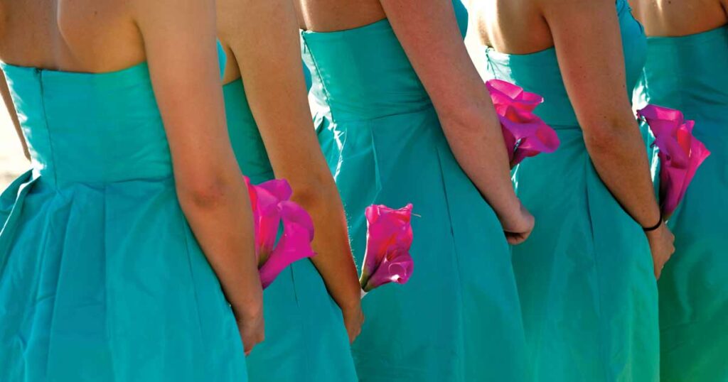 Cropped image of women lined up in bridal party all wearing teal dresses and carrying magenta colored calla lillies.