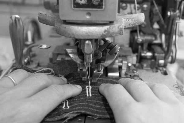 Greyscale image of person making a buttonhole in a suit on a professional sewing machine.
