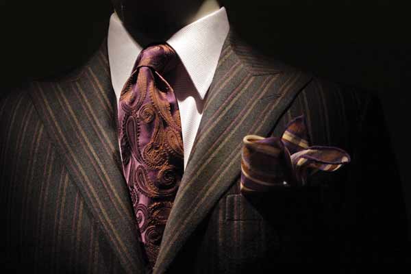 Close up of the top torso of a man wearing a fancy brown pin-striped suit. He has a paisley tie and matching handkerchief.