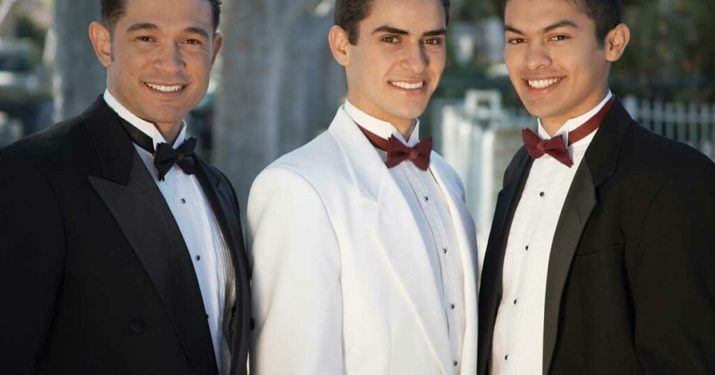Three men in tuxedos smiling at camera.