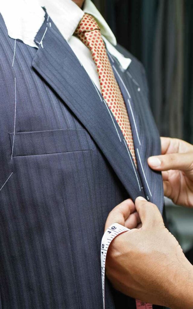 Close up image of person's hands altering a man's suit.