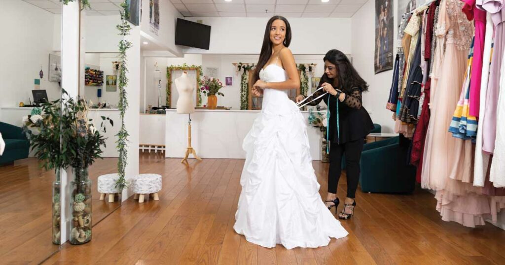Expert tailor working on alterations on woman wearing a white wedding dress.