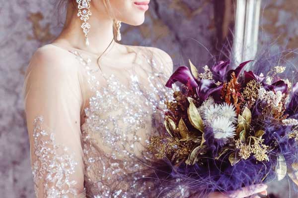 Bride wearing a sparkly hand-sewn sequin gown holding a bouquet of various purple flowers.