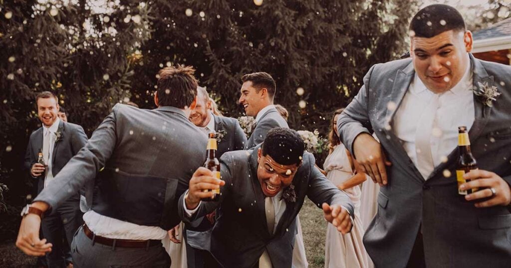 Groomsmen in suits celebrating with champayne, the bubbles are all over as if it's snowing. They are having a great time.